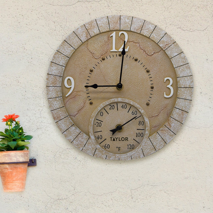 Outdoor terra cotta stone clock with thermometer, circular beige face mounted on a textured wall beside a potted plant