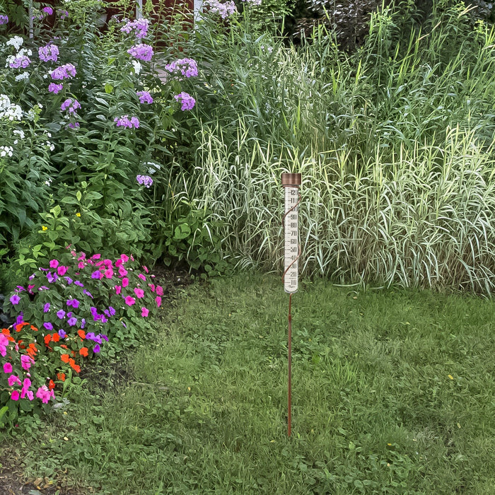 27 inch glass rain gauge with a brown cap standing in a garden among blooming flowers