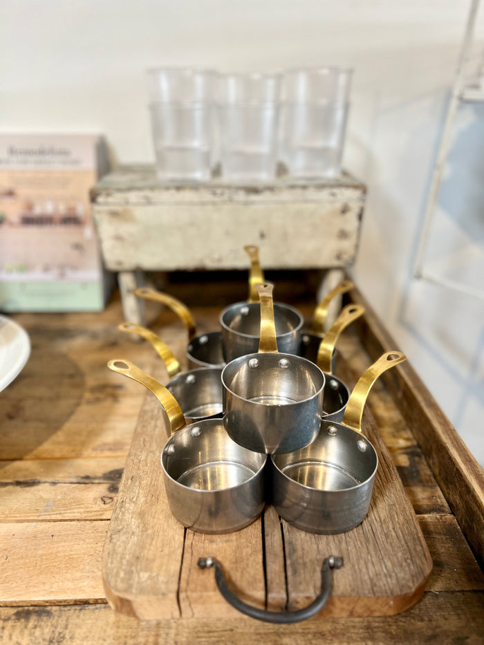 Small metal sauce pan set with gold handles on wooden stand