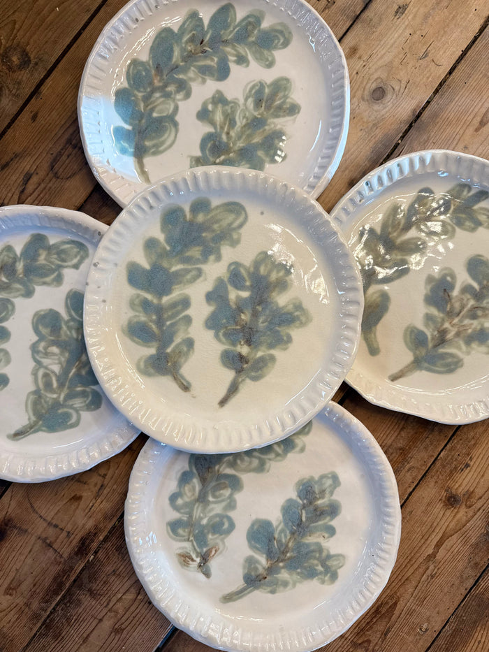 Set of five round white plates with scalloped rim and blue-green botanical leaf pattern