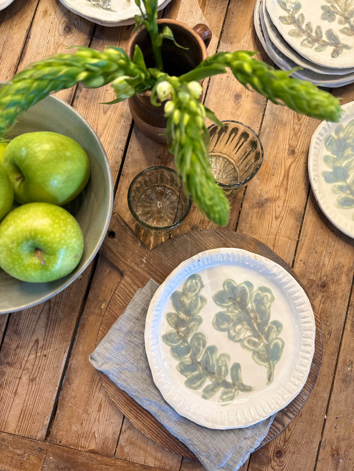 Round white plate with scalloped rim and blue-green botanical leaf pattern