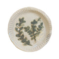 Round white plate with scalloped rim and blue-green botanical leaf pattern