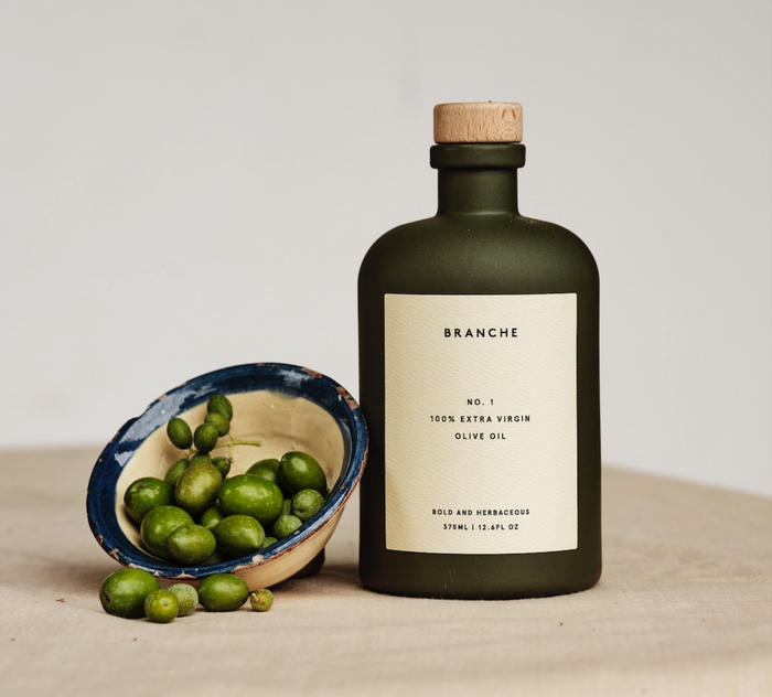Extra virgin olive oil bottle with cork top and label; small bowl of green olives