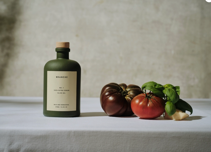 Extra virgin olive oil bottle beside tomatoes, eggplants, and basil on a table
