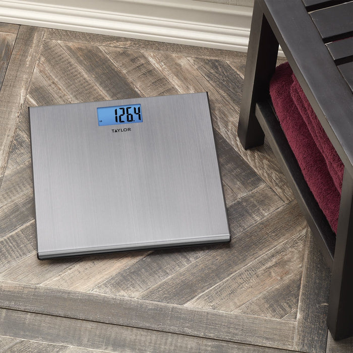 Slim brushed stainless steel digital scale on a wooden floor displaying 126.4 lb