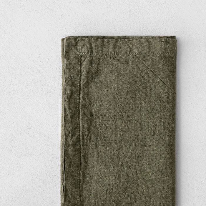 Olive green linen napkin with stitched border and flat folded surface