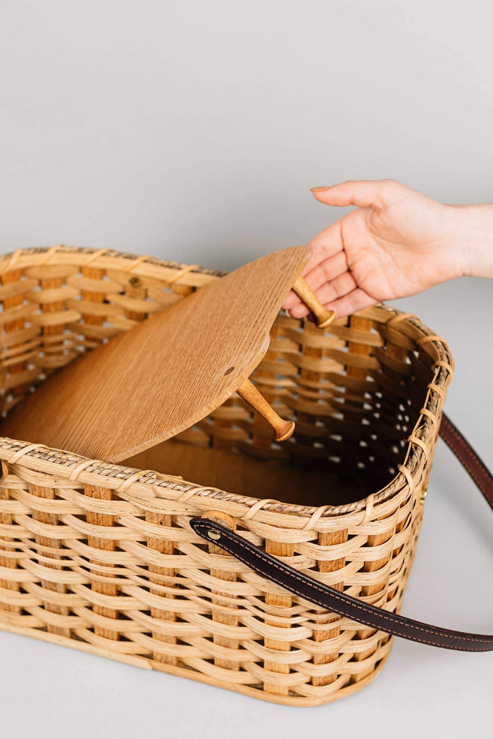 Open handwoven wicker picnic basket with wooden lid and dark leather strap handle