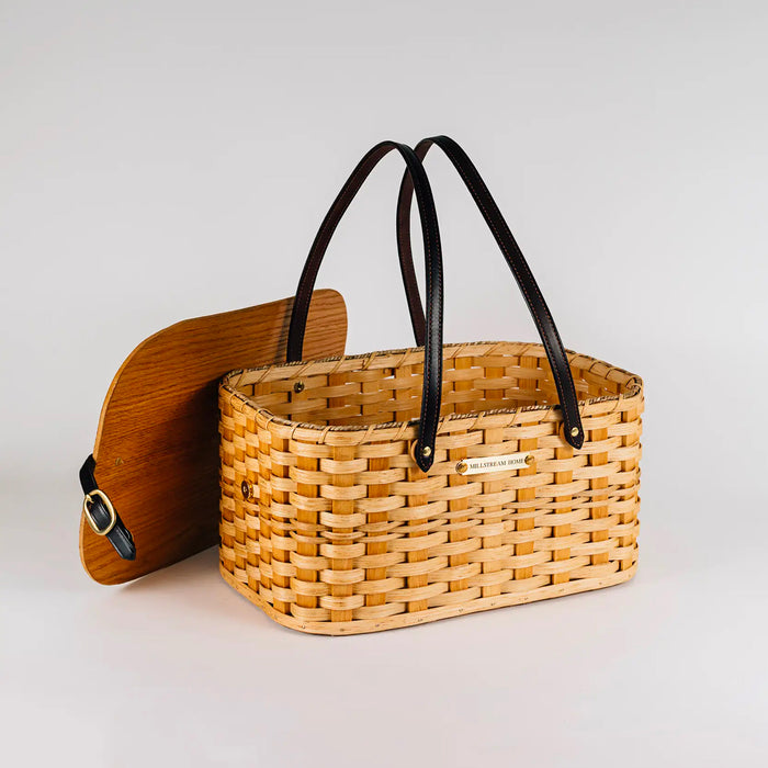 Handwoven wicker picnic basket with dark leather handles, side latch, and wooden lid
