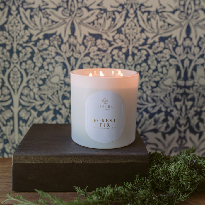 Scented candle in frosted white jar, Forest Fir label, flame burning