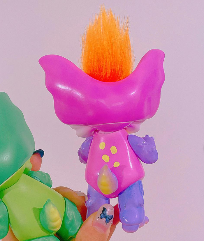 Two Little Bunny Dinosaur toy figurines by Vivian Wang, featuring oversized ears and fluffy hair, held in hand with a butterfly nail decal.