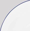A close-up shows the Raynaud Monceau Bleu Outremer Dinnerware—a white ceramic plate with a thin ultramarine blue rim—set against a light gray background, with only part of the plate visible.