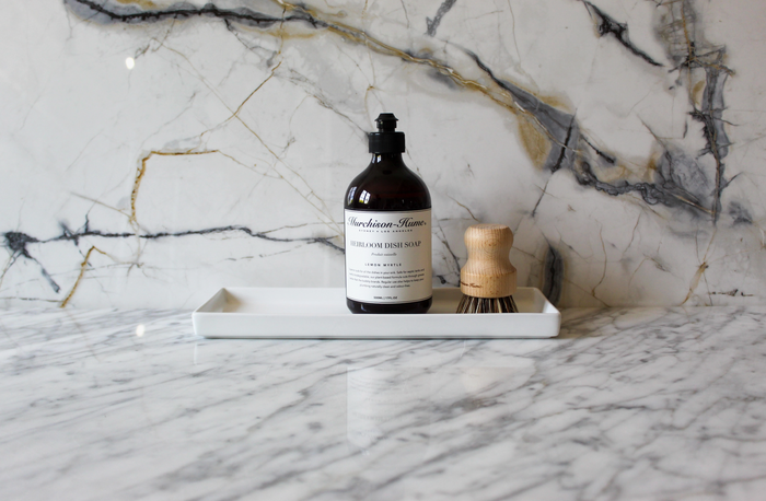 Heirloom dish soap bottle with black pump and amber liquid on a marble tray