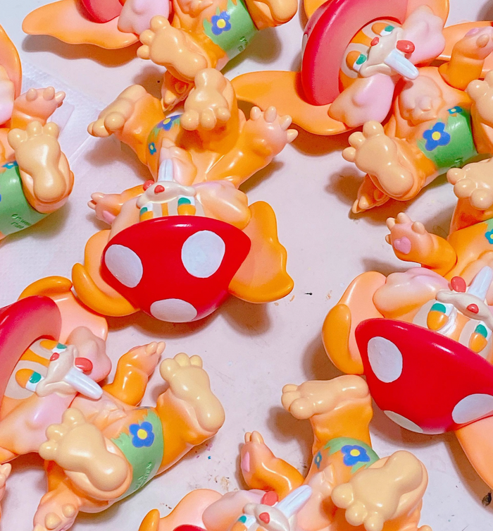 Mushroom by Vivian Wang: Chubby, orange vinyl art-toys with floppy ears, green floral shorts, and polka-dot mushroom caps, unassembled, lying on their backs.